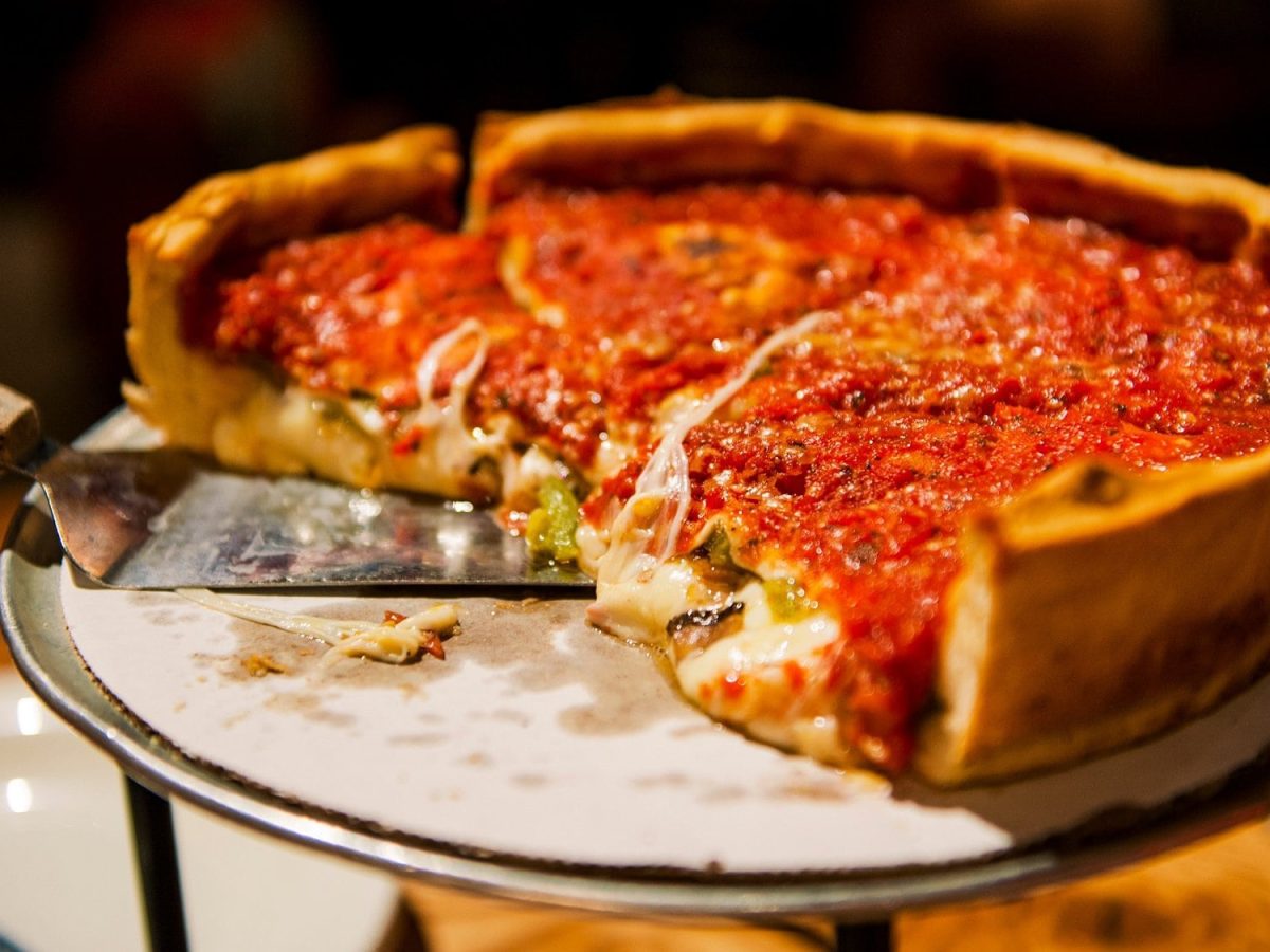 Eine angeschnittene Chicago Deep Dish Pizza mit Käse gefüllt und Tomatensauce bedeckt, auf einem Pizzaständer.