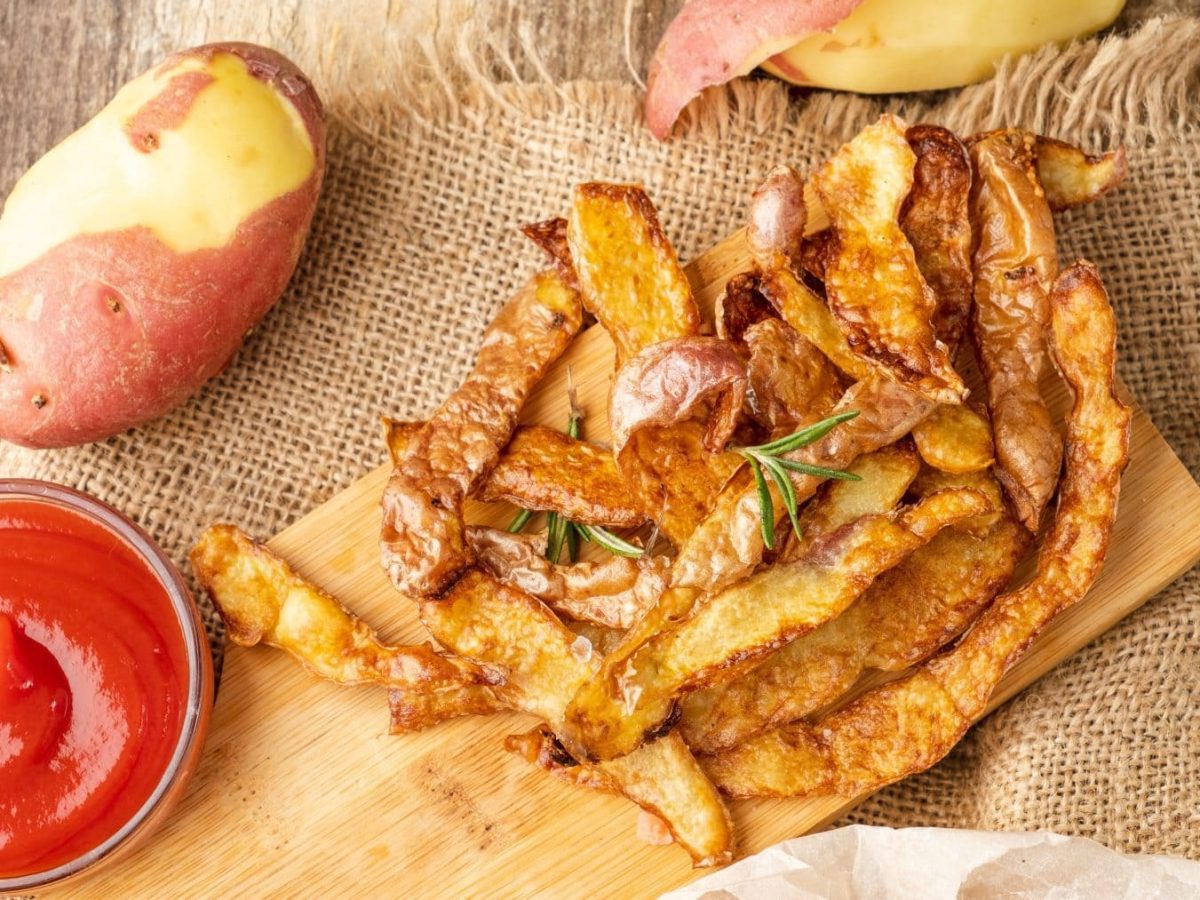 Chips aus Kartoffelschalen mit Kartoffeln und Ketchup auf Holzbrett auf einem Tuch. Draufsicht.