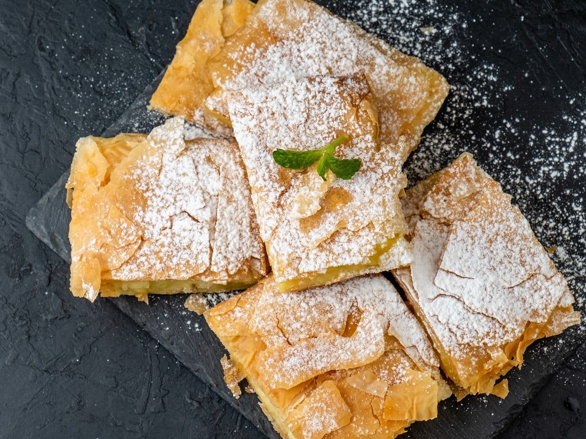 Mehrere Stücke Bougatsa auf einer schwarzen Schieferplatte