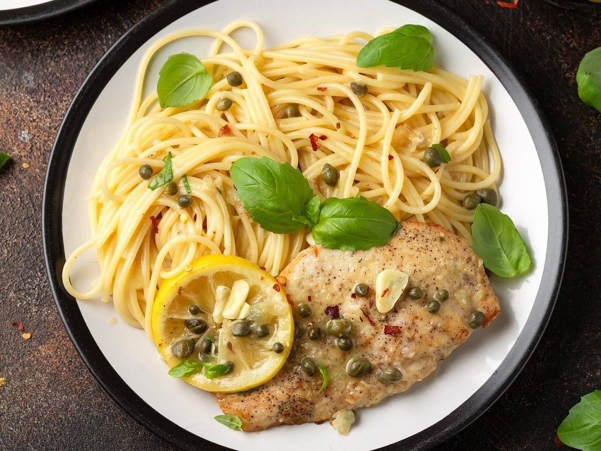 Ein Teller mit Chicken Piccata auf einem Holztisch.