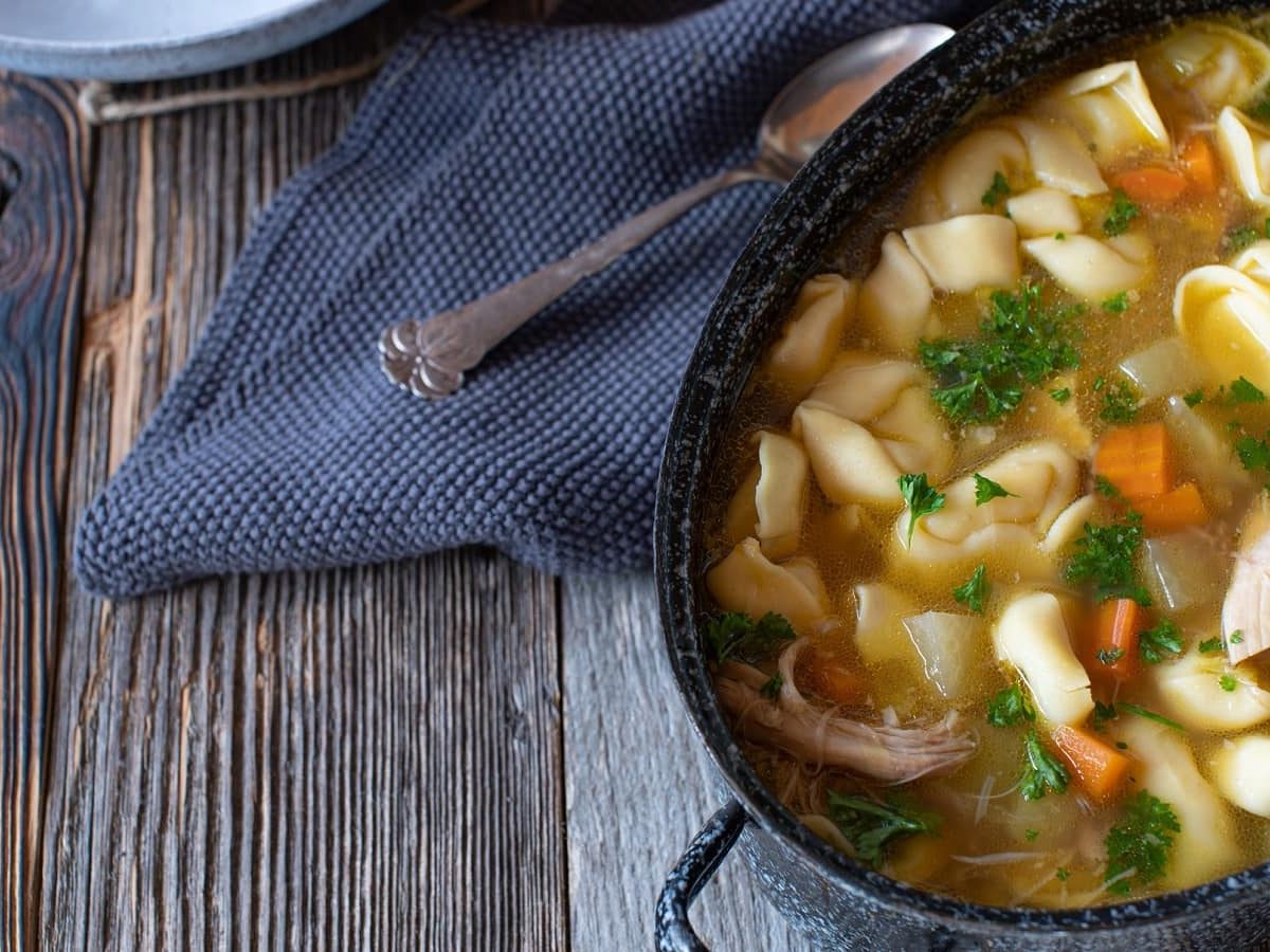 Ein Topf mit Hühnersuppe mit Tortelloni auf einem Holztisch.