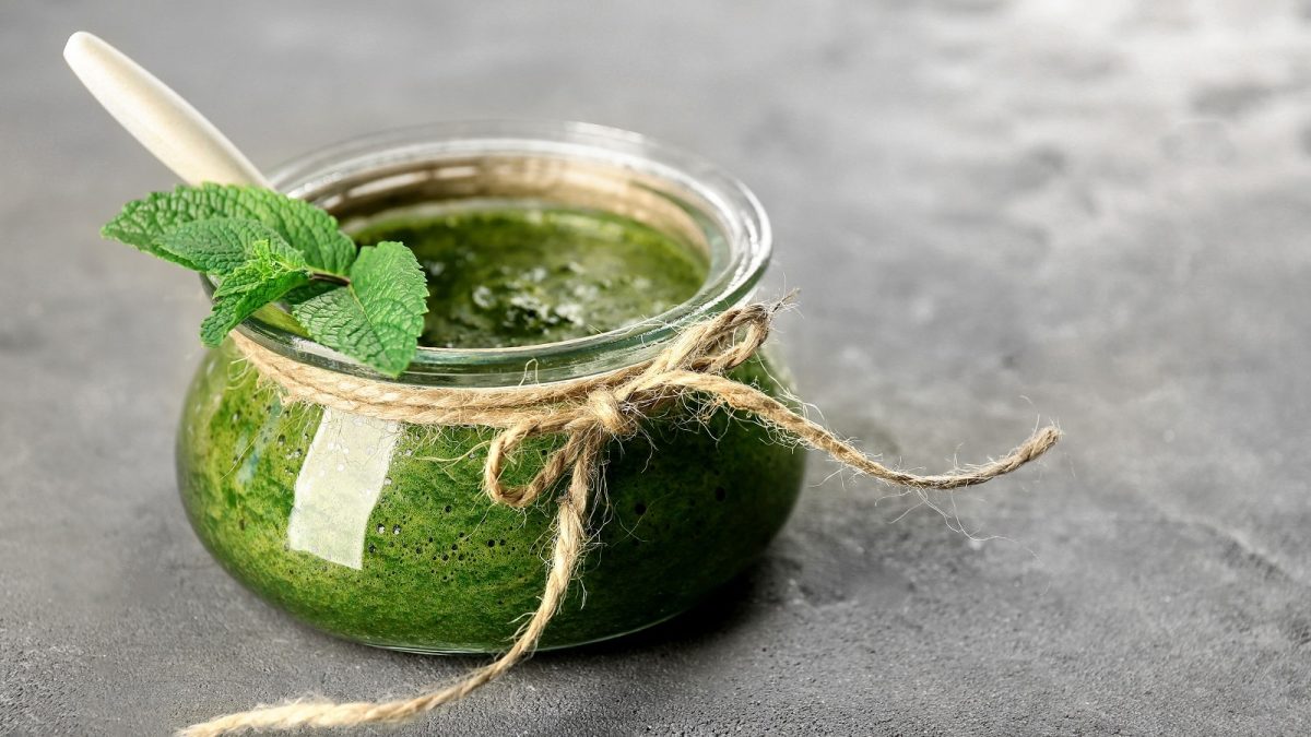 Ein Glas mit Minz-Pesto auf einem grauen Tisch.