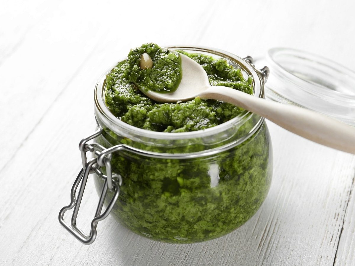 Ein Glas mit Rosenkohl-Pesto auf einem weißen Holztisch.