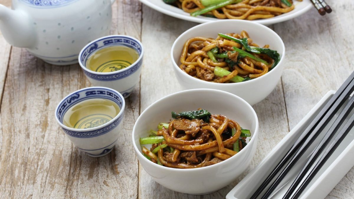 Zwei Schüsseln mit Shanghai-Style Nudeln neben Stäbchen und Tee.