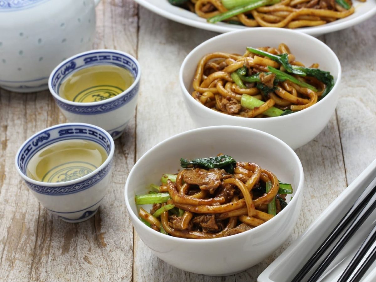 Zwei Schüsseln mit Shanghai-Style Nudeln neben Stäbchen und Tee.