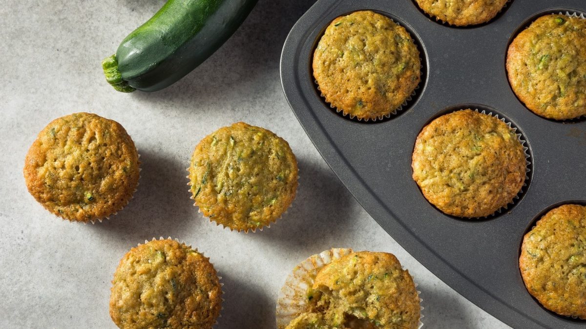 Ein Blech mit Zucchinibrot-Muffins neben einer frischen Zucchini.