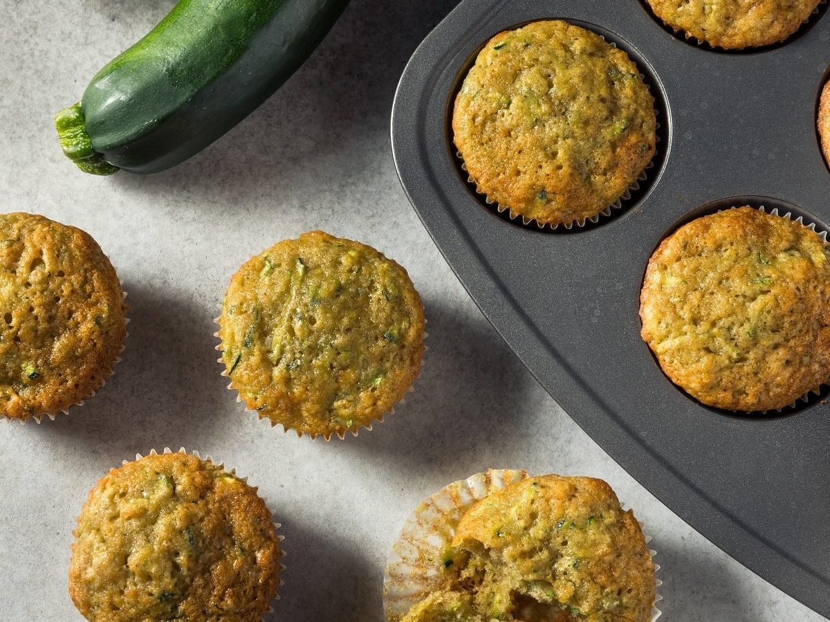 Ein Blech mit Zucchinibrot-Muffins neben einer frischen Zucchini.