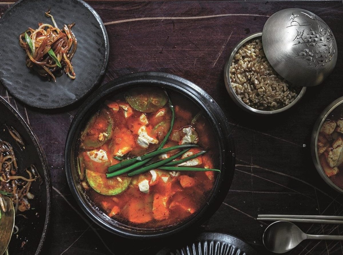 EIn Eintopf mit Seidentofu und Frühlingszwiebeln in der Draufsicht, daneben Teller und Schalen mit weiteren koreanischen Speisen.