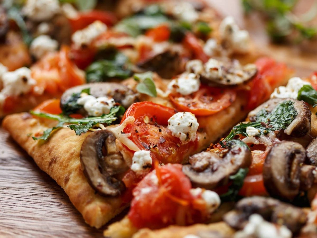 Eine in Stücke geschnittene Flatbread Pizza mit Pilzen, Tomaten, Rucola und Fetakäse.