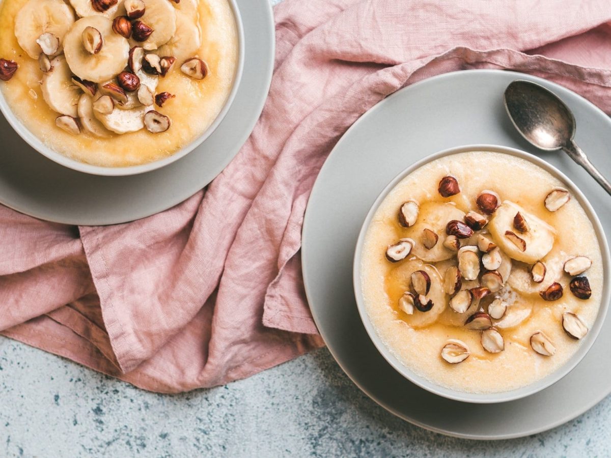 Zwei Schüsseln Frühstücks-Polenta mit karamellisieren Bananen und Haselnüssen in der Draufsicht.