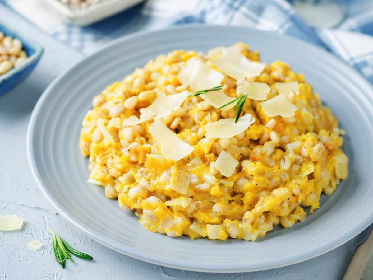 Graupenrisotto mit Kürbis und frisch geriebenem Parmesan, serviert auf einem grauen Teller auf hellem Untergrund.