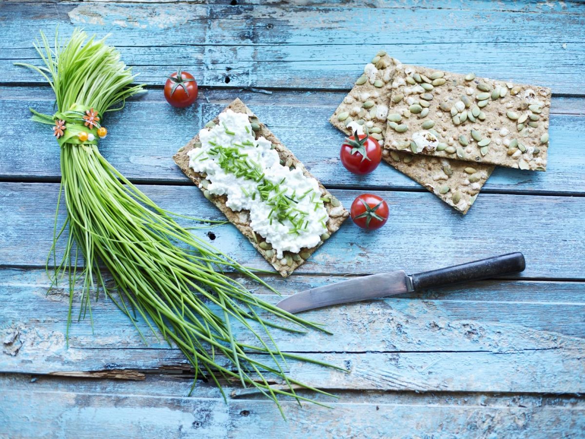 Draufsicht: Auf einem blauen Untergrund aus Holz liegen Knäckebrot mit Frischkäse, Schnittlauch und Cocktailtomaten