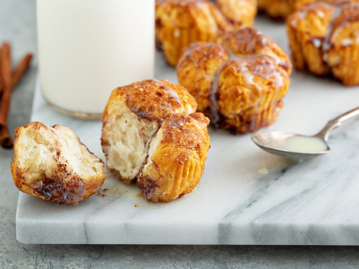 Eine weiße Amrmorplatte mit den Monkey-Bread-Muffins. Im Hintergrund sind unscharf eine Karaffe mit Sahne und ein paar Zimtstangen zu erkennen.