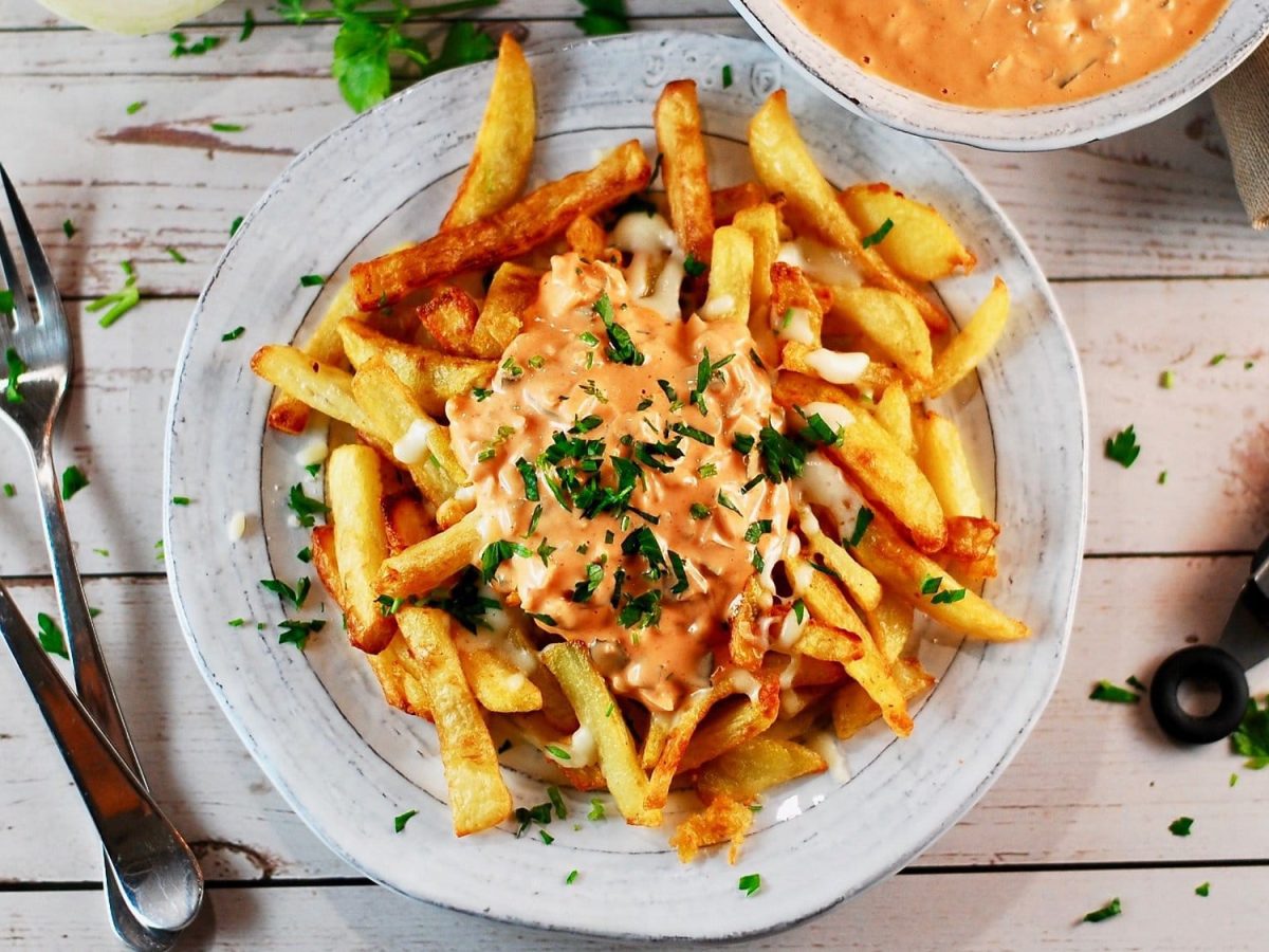 Ein Teller Poutine mit veganer Bratensauce und Petersilie, daneben zwei Gabeln, alles Draufsicht.