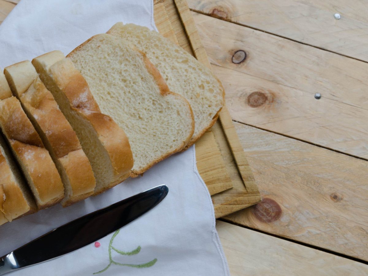 Selbst gemachtes Toastbrot aufgeschnitten auf Holzbrett und Holztisch. Daneben Buttermesser. Draufsicht.