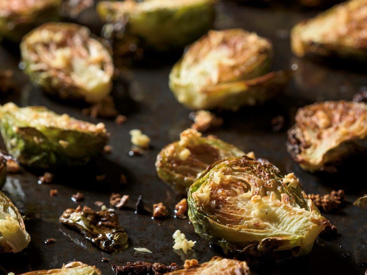 Smashed Rosenkohl mit Honig-Limetten-Glasur auf schwarzem Untergrund. Draufsicht.