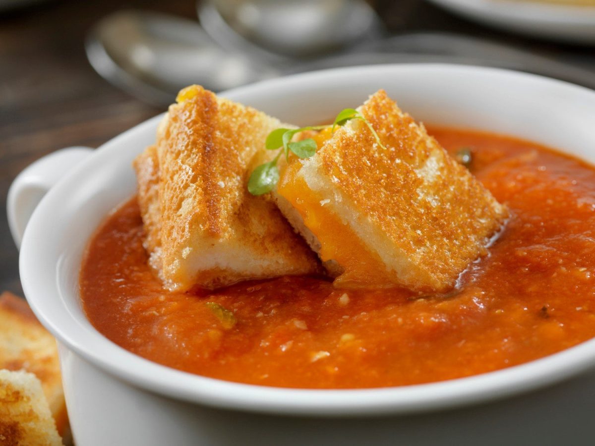 Tomaten-Paprika-Suppe mit Grilled Cheese Croutons in weißer Suppenschüssel. Draufsicht.