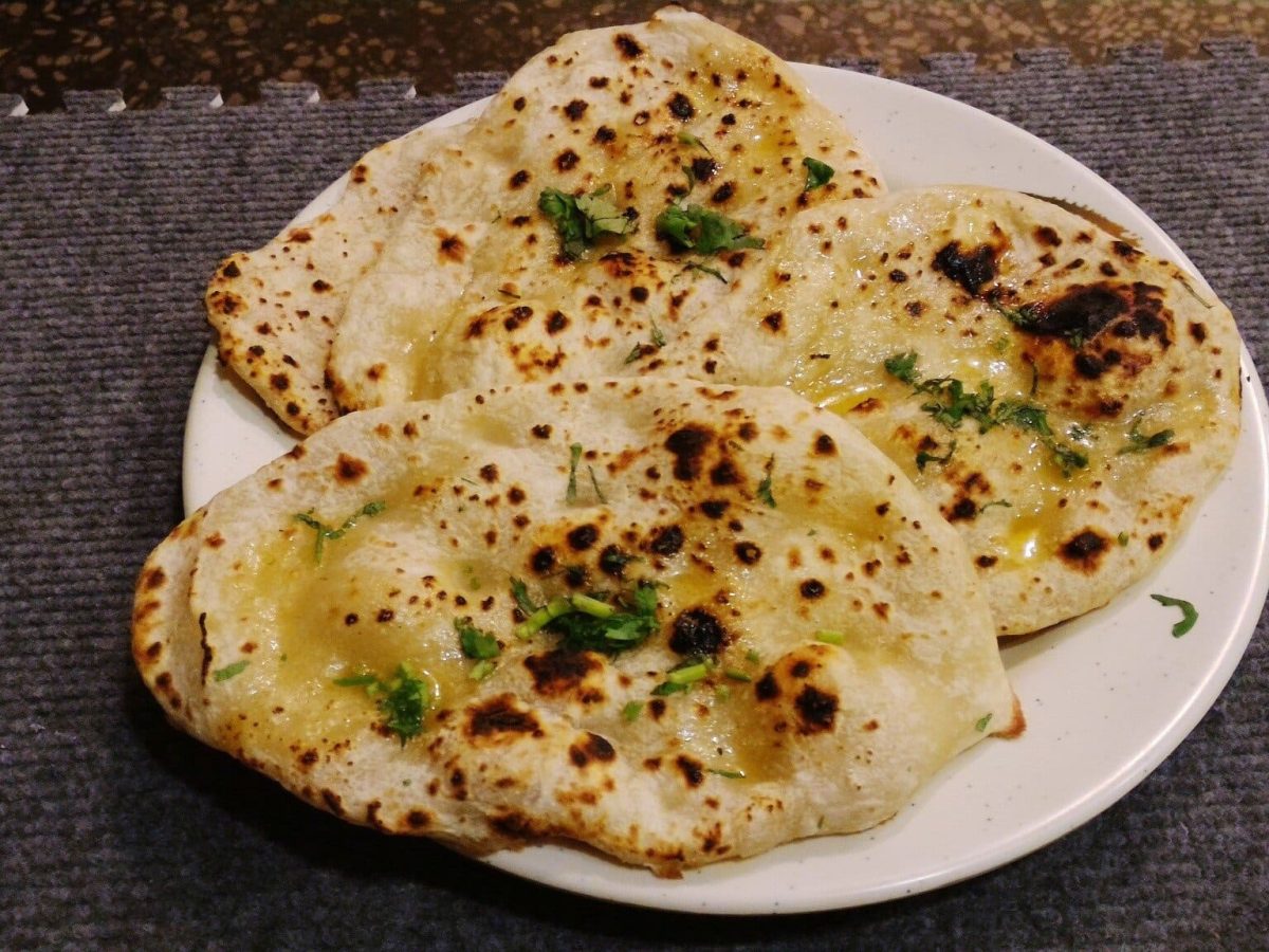 Stuffed Flatbread mit Käse und Kräuterbutter auf weißem Teller und dunklem Untergrund. Draufsicht.