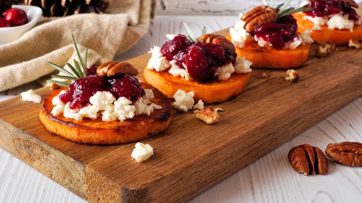 Süßkartoffel-Häppchen mit Cranberry-Kompott und veganem Feta sowie Pecannüssen auf einem Holzbrett