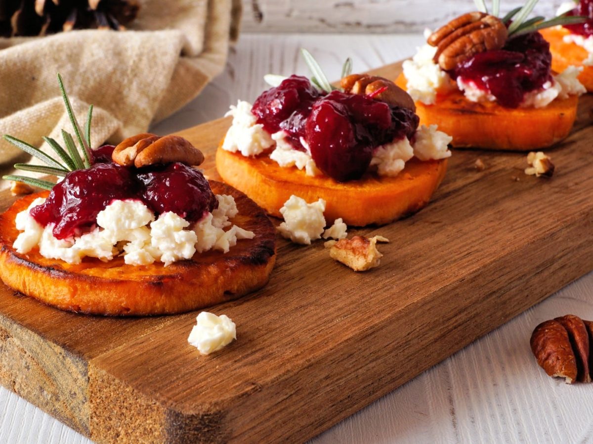 Süßkartoffel-Häppchen mit Cranberry-Kompott und veganem Feta sowie Pecannüssen auf einem Holzbrett