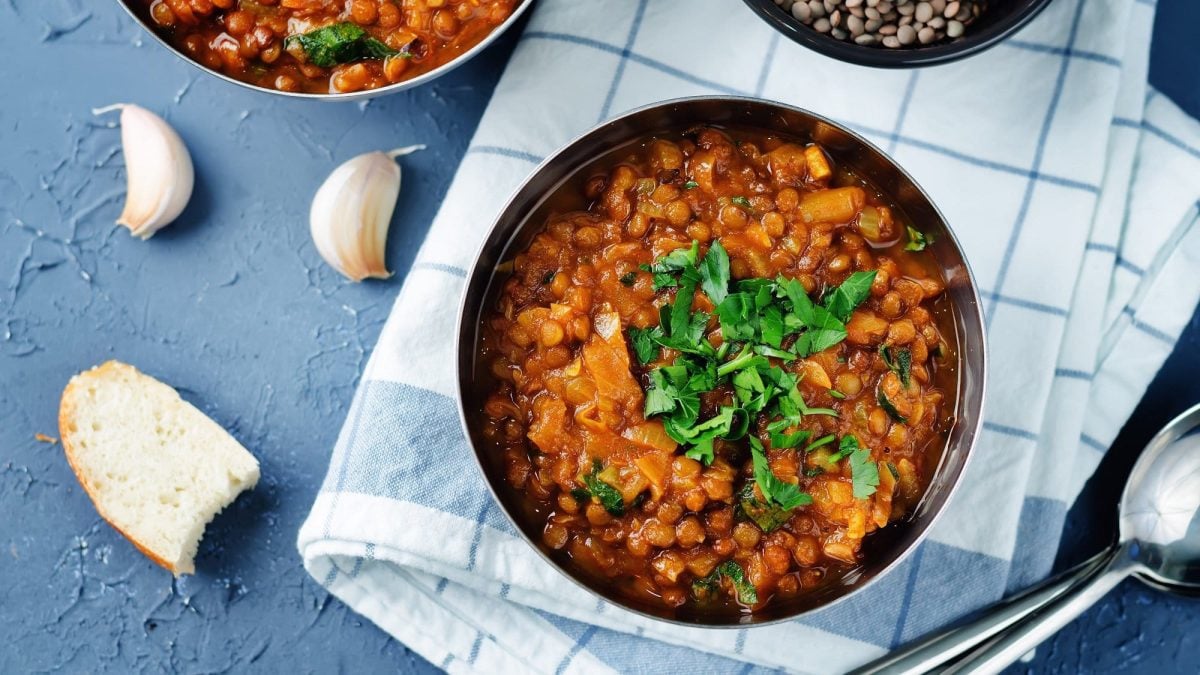 Eine Schüssel veganer Linseneintopf mit Petersilie in der Draufsicht, daneben Knoblauch und Brot.