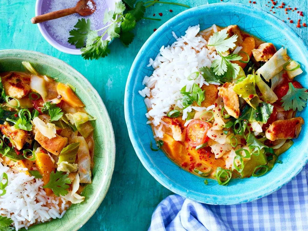 Draufsicht: Türkise Untergrund mit zwei Schüsseln gefüllt mit Reis und einem bunten Weißkohl-Hähnchen-Curry