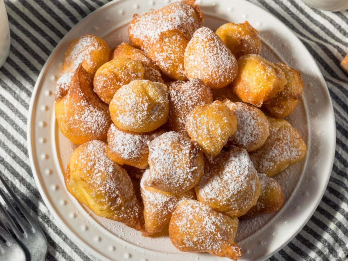 Teller mit Zeppoli di Patate und Puderzucker auf einem gestreiften Küchentuch in der Draufsicht.