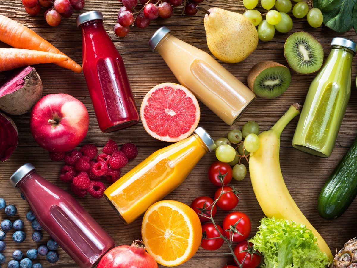 Drauf sicht auf bunte Flaschen mit Saft und frisches Obst auf einem Holztisch.