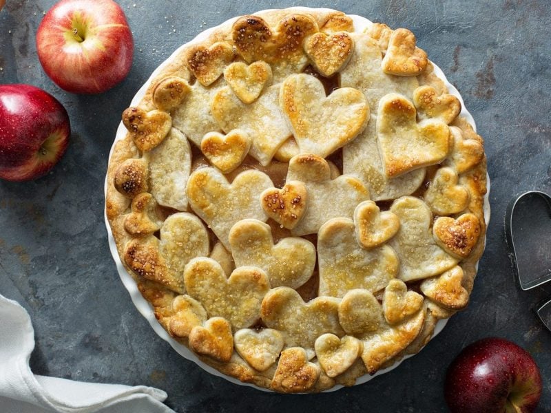 Auf einem Teller ist ein Apfel-Gitterkuchen mit Herzen serviert. Der Teig ist herzförmig gestaltet.