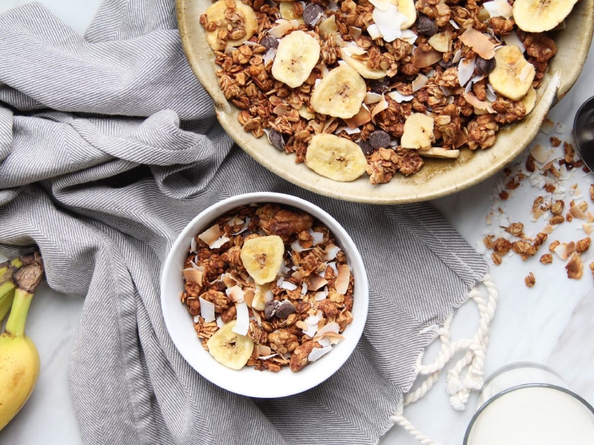 Eine weiße Schale mit dem Bananen-Granola auf hellgrauem Untergrund.