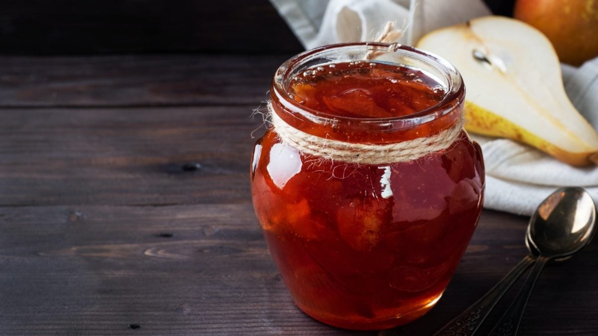 Dunkler Untergrund. Im Vordergrund ein Glas mit Birnen-Tonka-Konfitüre. Im Hintergrund eine weißes Leinentuch mit einer aufgeschnittenen Birne.