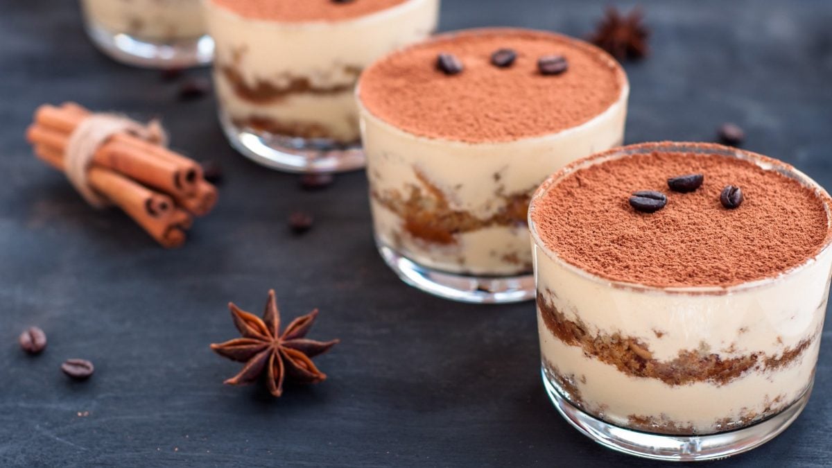 Vier Gläser Biscoff-Tiramisu mit Kekskrümeln, daneben Sternanis und Zimtstangen.