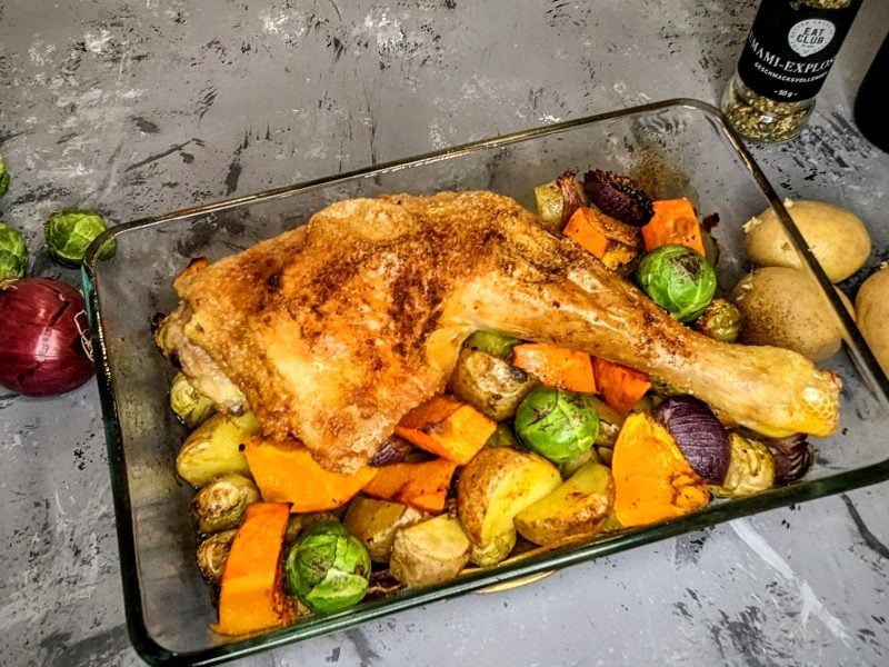 Eine Glas-Auflaufform mit dem Paprikagewürz-Hähnchen, Rosenkohl und Kürbis auf einem grauen Tisch.