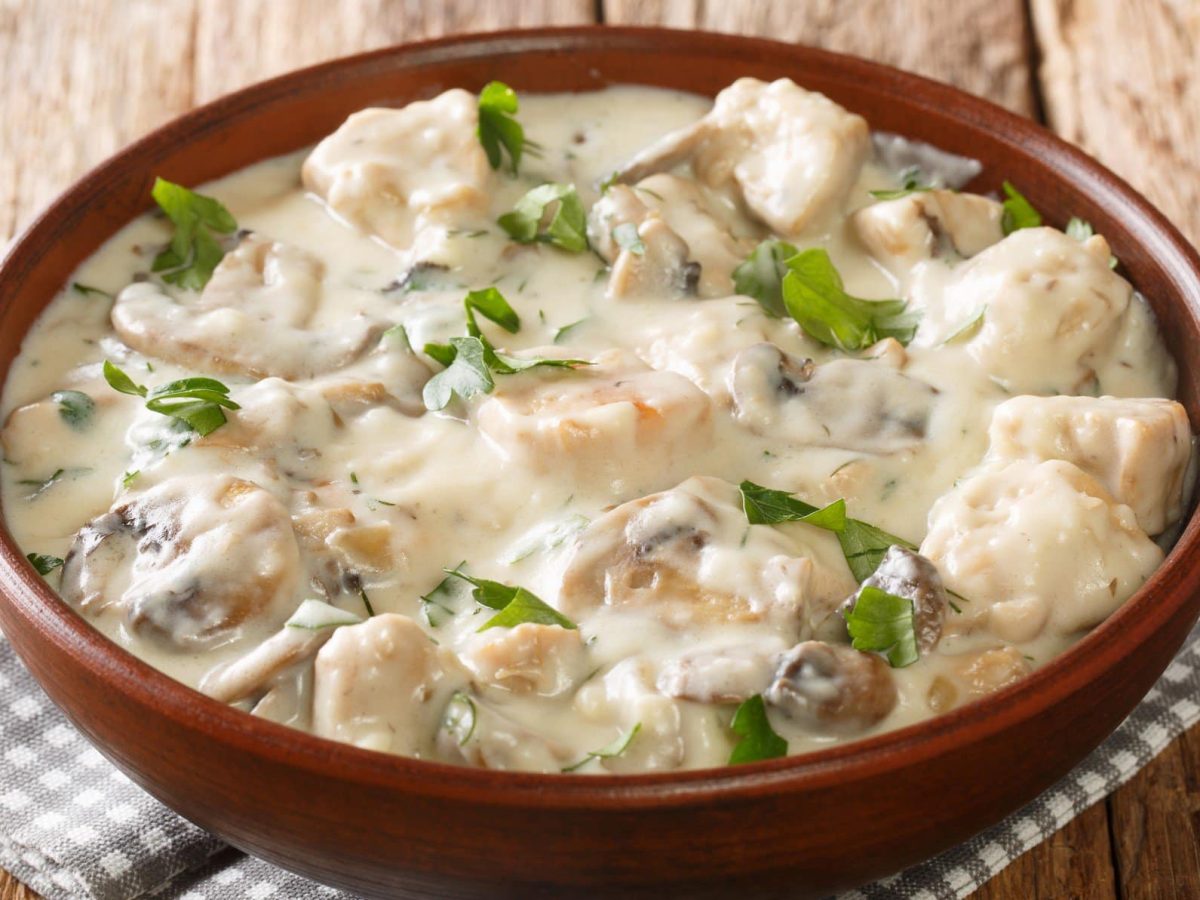 Eine braune Schale mit dem Hähnchenragout auf einem Holztisch.