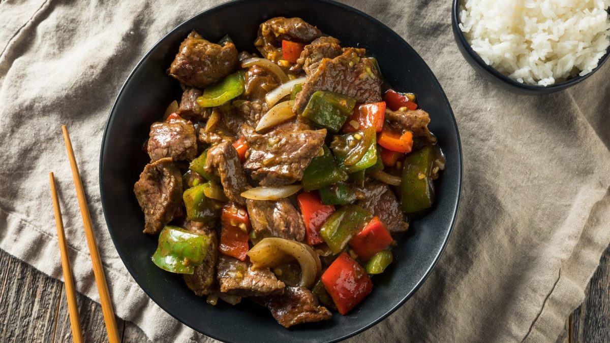 Ein schwarzer Teller mit Cumin Beef auf einem gedeckten Tisch.