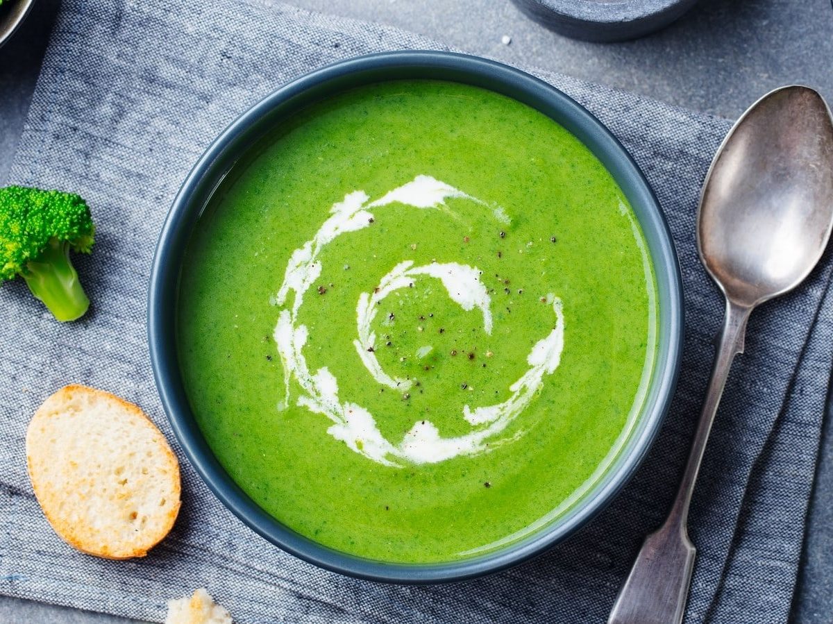 Eine Schüssel Green Goddess Suppe neben frischen Zutaten.