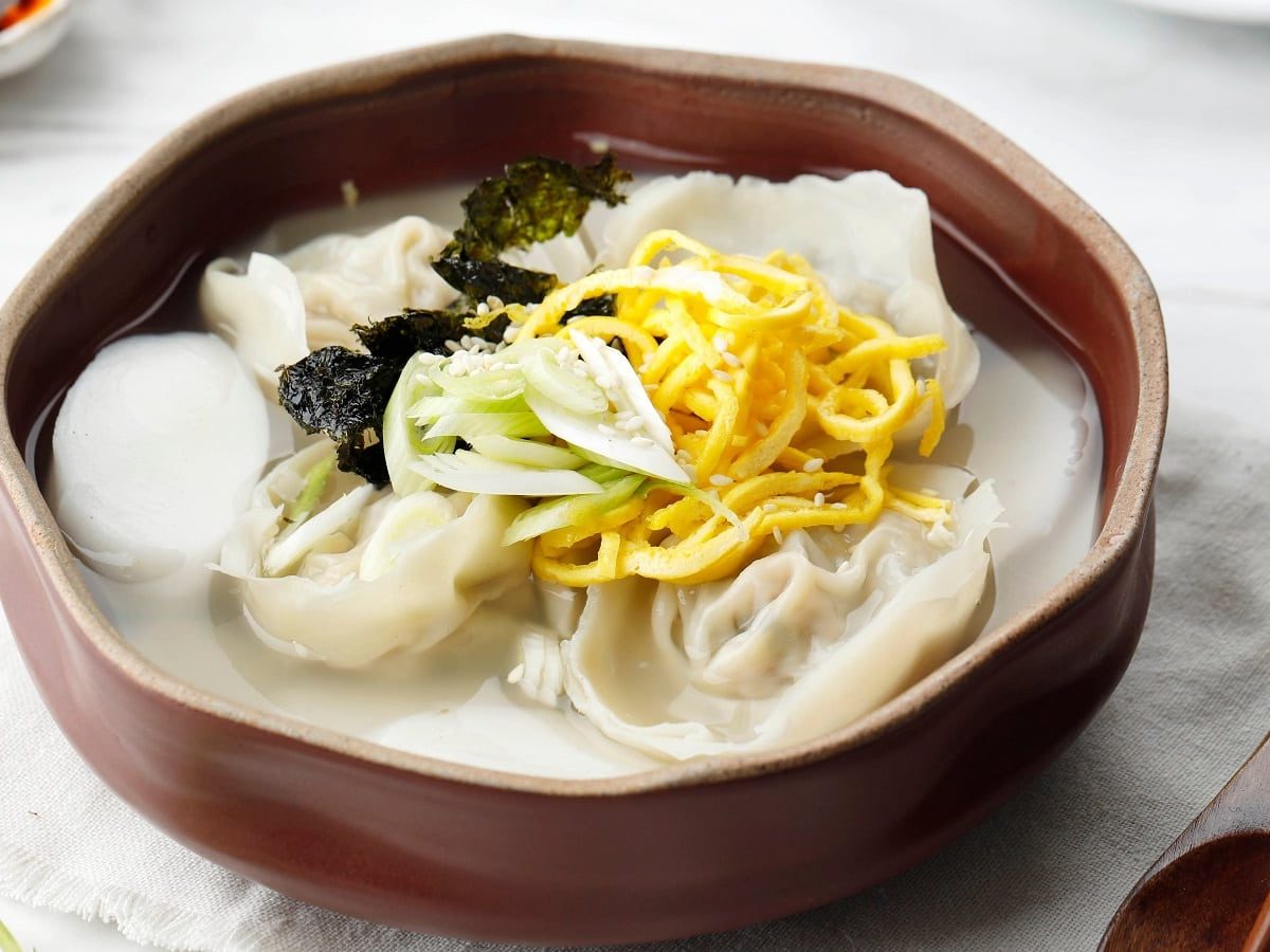 Eine Holzschüssel mit Mandu-Suppe auf einem weißen Tisch.