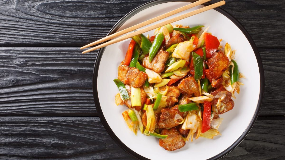 Ein weißer Teller mit Sichuan Schweinebauch auf einem schwarzen Tisch.