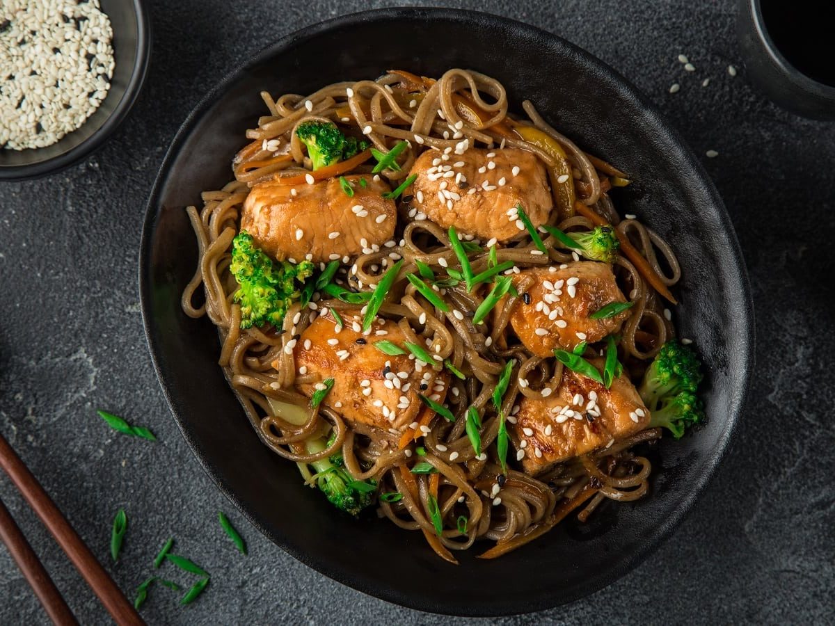 Ein schwarzer Teller mit Soba-Nudeln mit Teriyaki-Lachs.