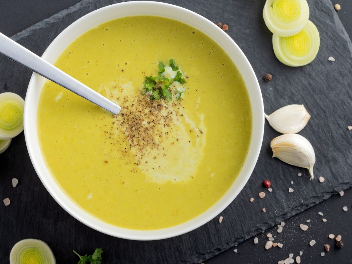 Eine weiße Schale mit der Lauchsuppe auf einer schwarzen Schiefertafel.