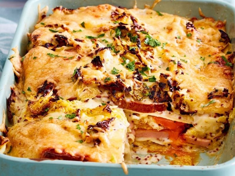 Fleischkäse-Lasagne mit Wirsingrahm in weißer Ofenform vor hellem Hintergrund.