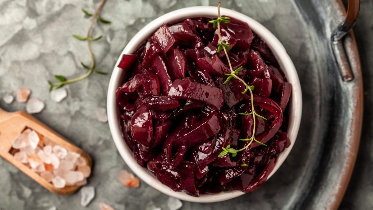 Draufsicht: Auf einem grauen Untergrund steht ein Glas Rotes Zwiebel-Confit. Daneben liegen rosa Salzkörner und frischer Thymian