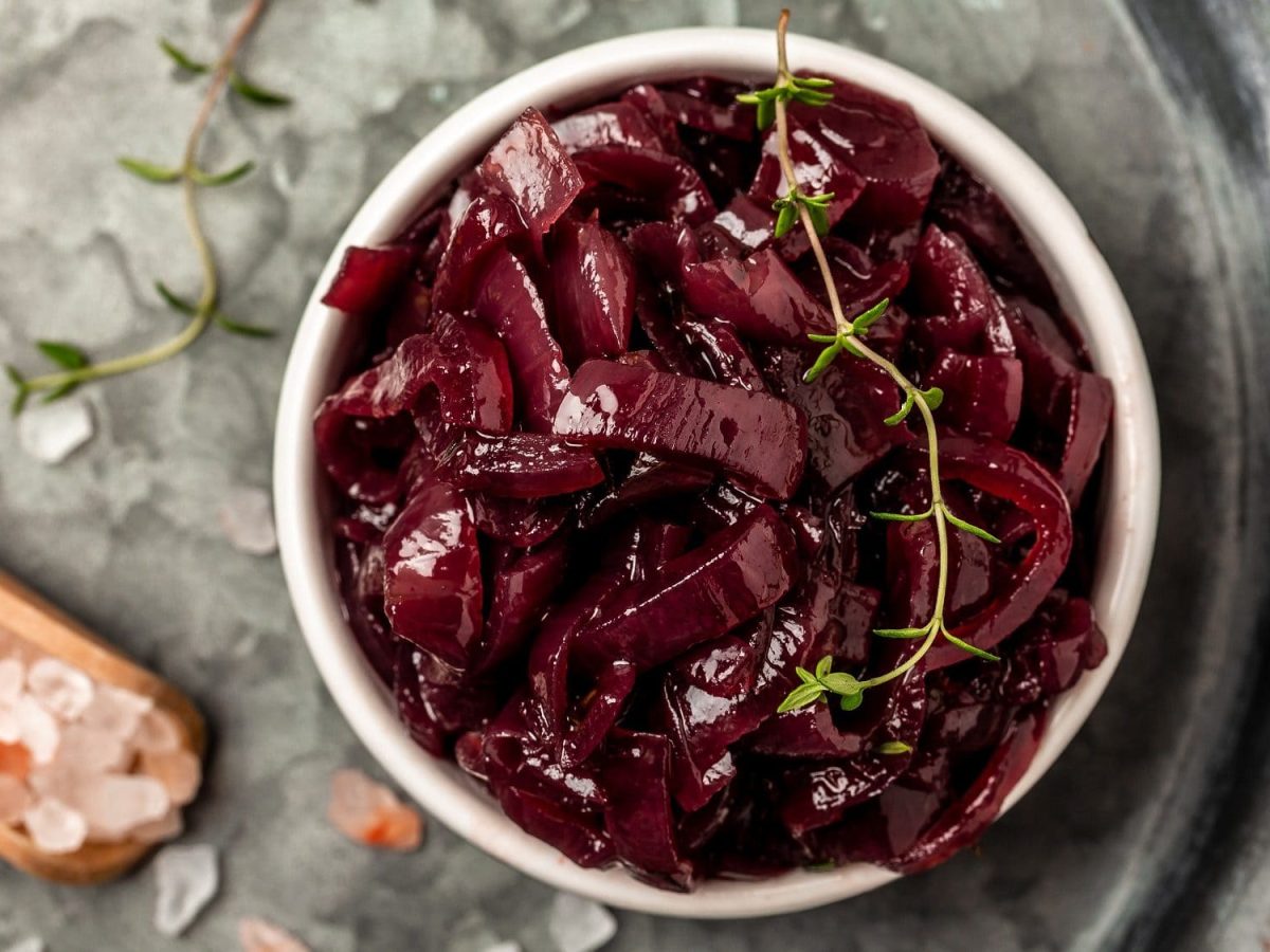 Draufsicht: Auf einem grauen Untergrund steht ein Glas Rotes Zwiebel-Confit. Daneben liegen rosa Salzkörner und frischer Thymian