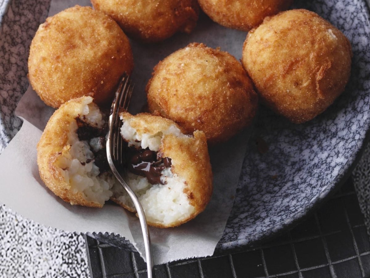 Frittierte Milchreisbällchen mit Schokoladenkern in einer Schüssel vor grauem Hintergrund.