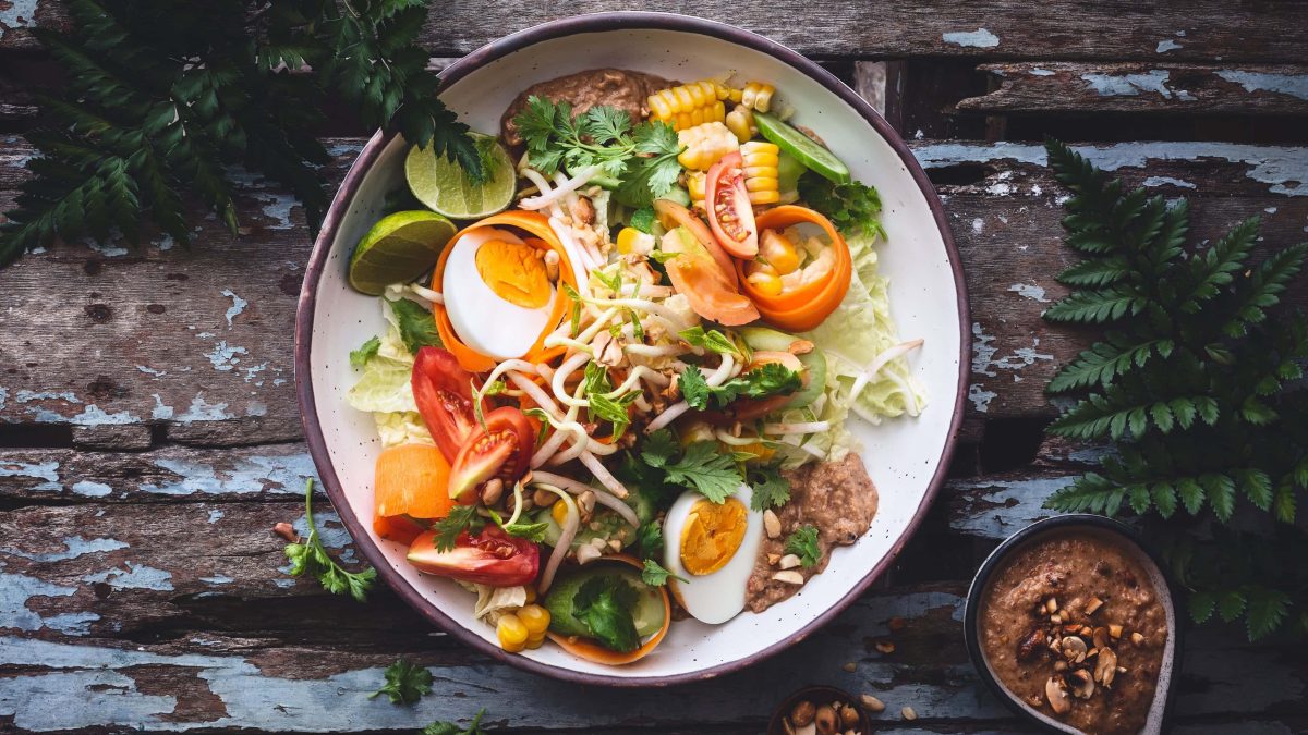 Eine bunte Gado-Gado-Bowl auf einem rustikalen Holztisch.