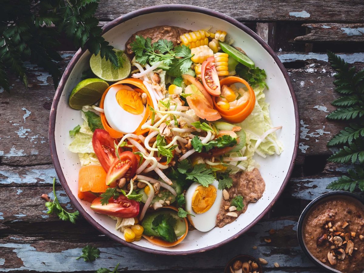 Eine bunte Gado-Gado-Bowl auf einem rustikalen Holztisch.