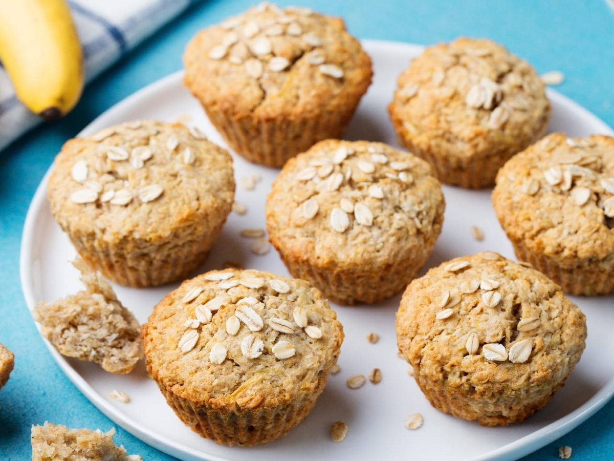 Mehrere Haferflocken-Muffins auf einem weißen Teller und blauem Untergrund.