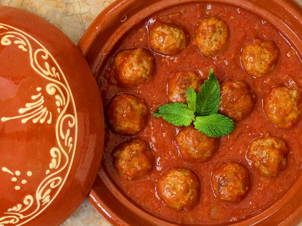 Marrokanische Fleischbällchen in einer Tomatensauce in einem Tontopf auf Marmorfliesen.