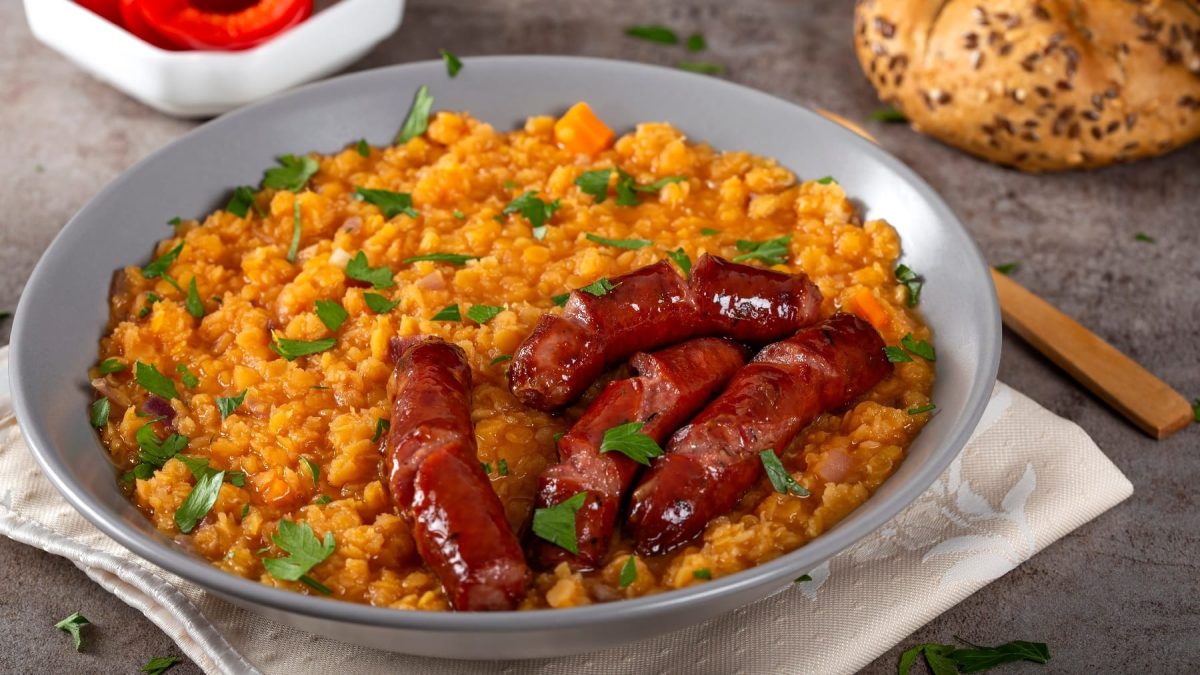 Ein graue, tiefer Teller mit der Linsensuppe und Chorizo auf einem grauen Steintisch.