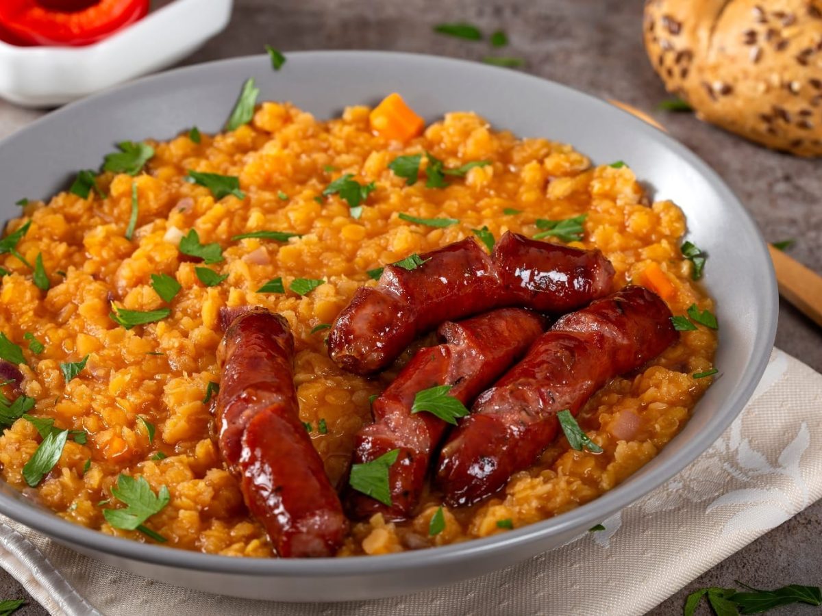 Ein graue, tiefer Teller mit der Linsensuppe und Chorizo auf einem grauen Steintisch.